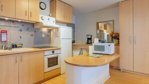 Eine moderne Küche mit Holzausstattung, einem Einbauofen, einer Mikrowelle und einer Uhr an der Wand.