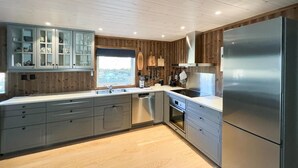 A modern kitchen with wooden paneling, stainless steel appliances, and a large window providing natural light.