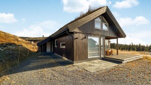 A modern wooden cabin with a sloped roof, large windows, and a stone pathway leading to the entrance.