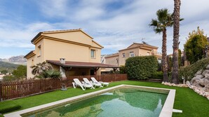 A swimming pool with lounge chairs, a wooden fence, and a house with a mountain view.