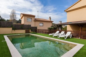 A swimming pool with a tiled edge, surrounded by a wooden fence, and a building with a tiled roof in the background. - Holiday Home 'Collbato Resort' with Mountain View, Wi-Fi and Air Conditioning (Collbato)