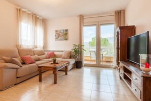 A living room with a sofa, a coffee table, a TV, and a balcony with a view. - Holiday Home 'Collbato Resort' with Mountain View, Wi-Fi and Air Conditioning (Collbato)