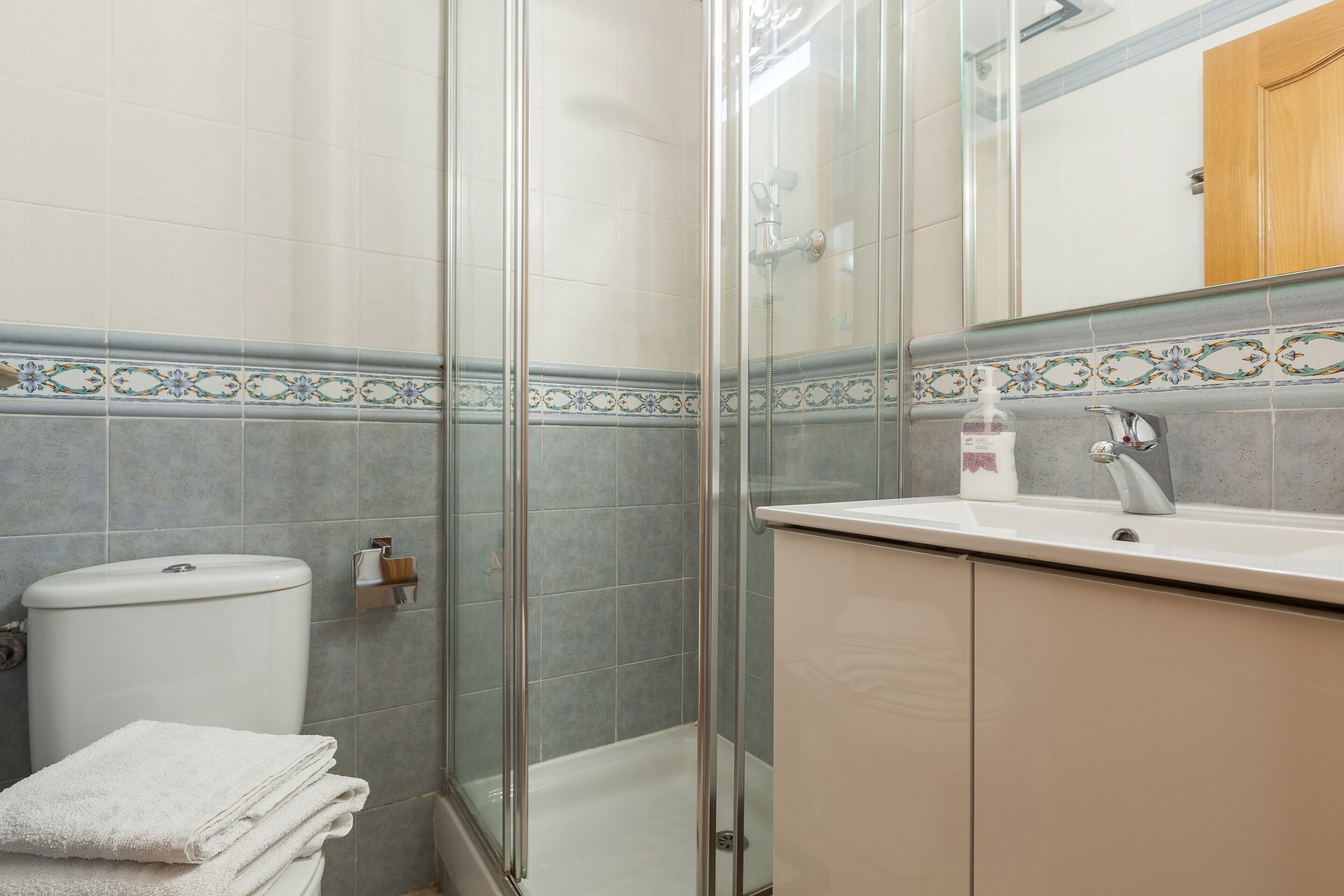 Une salle de bain avec une douche à parois de verre, des toilettes, un lavabo avec un miroir et une pile de serviettes.