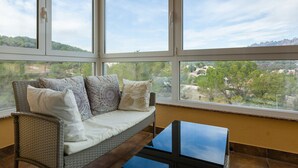 A room with a wicker sofa, a glass coffee table, and large windows offering a view of a green landscape.