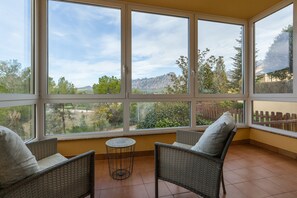 A room with large windows, wicker furniture, and a small round table. - Holiday Home 'Collbato Resort' with Mountain View, Wi-Fi and Air Conditioning (Collbato)