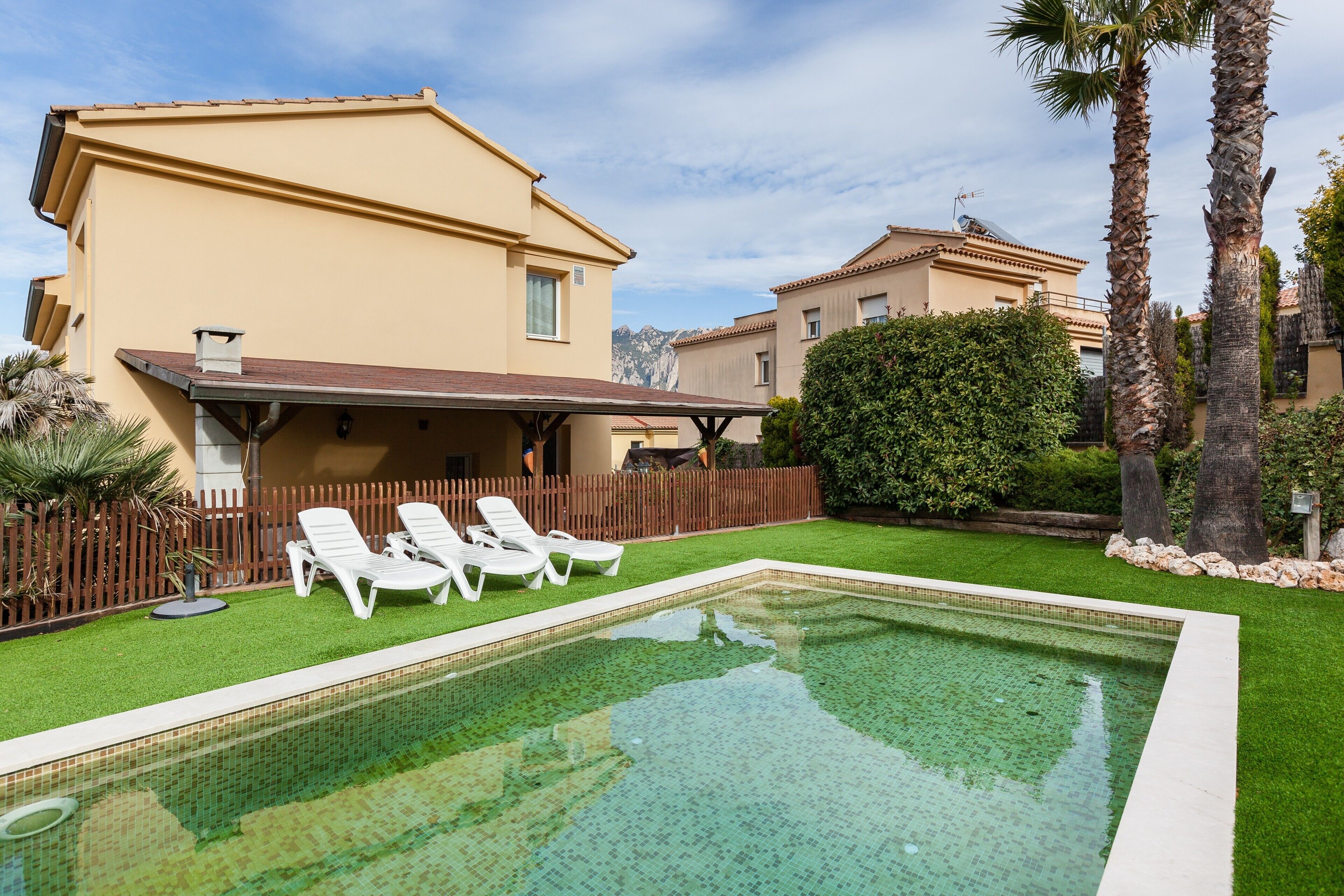 A swimming pool with lounge chairs, a wooden deck, and a building with a beige facade.
