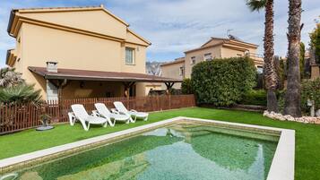 A swimming pool with lounge chairs, a wooden deck, and a building with a beige facade.