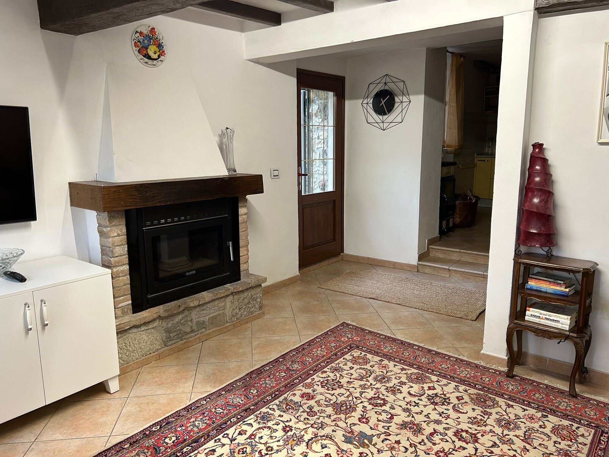 A living room with a fireplace, a TV, a bookshelf, and a patterned rug.