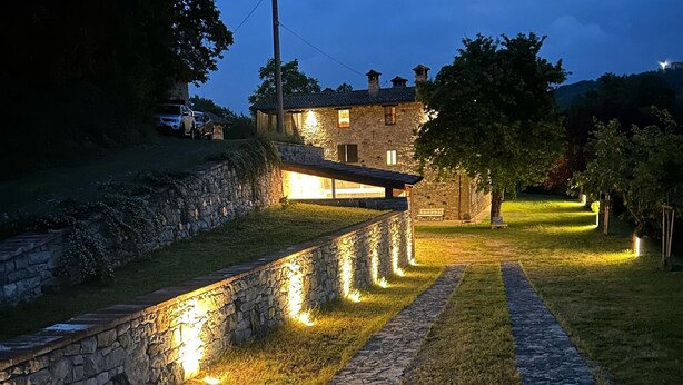 Un chemin de pierre mène à un bâtiment en pierre doté d’un toit en pente et de plusieurs cheminées.