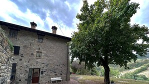 Un bâtiment en pierre avec une porte rouge, un banc et un grand arbre dans une cour.