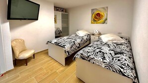 Une chambre avec deux lits, une chaise, une armoire, un téléviseur à écran plat et un tableau.