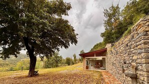 Un bâtiment en pierre doté d’une structure en verre, entouré d’un mur de pierre et d’un arbre.