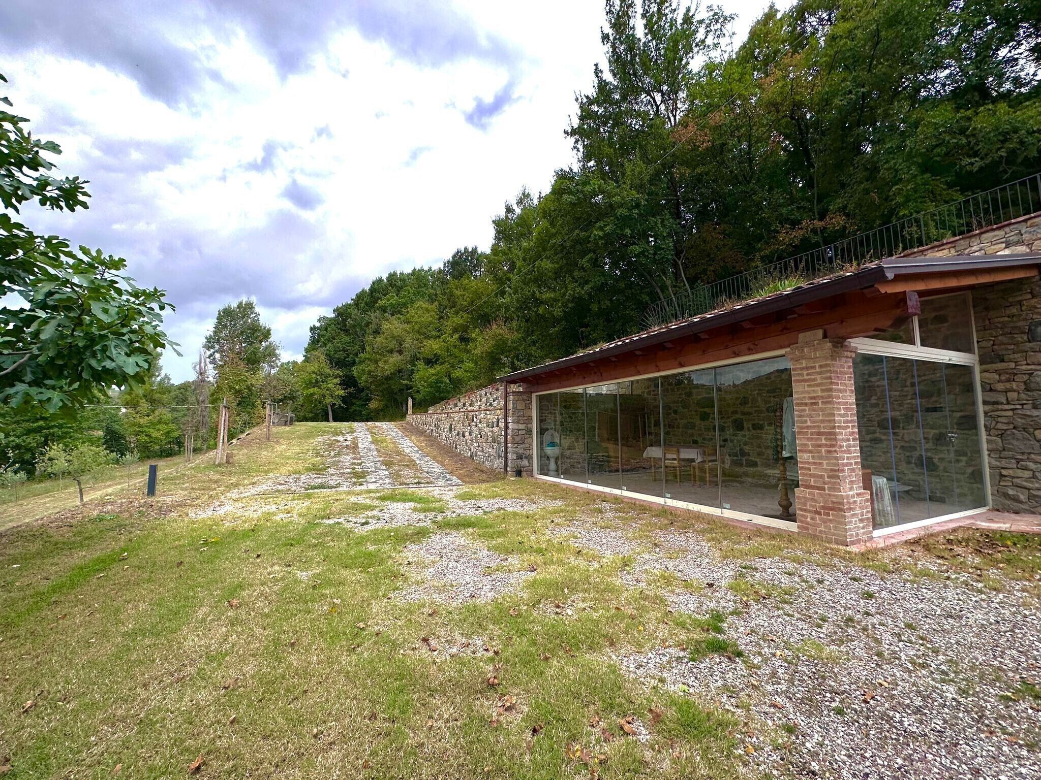 A modern building with a stone exterior, large glass windows, and a gravel pathway leading to a wooden deck.