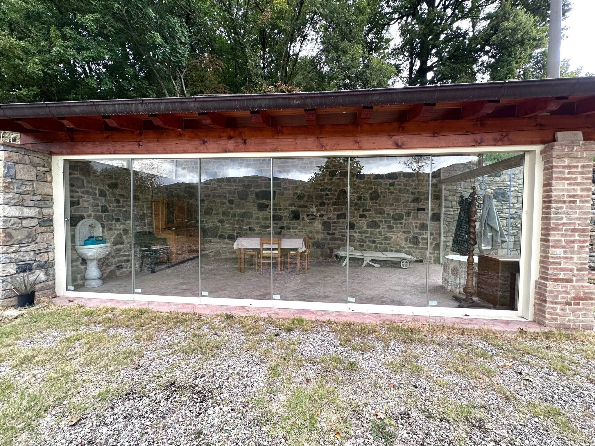 Eine moderne, verglaste Terrasse mit einer Steinwand, einem Holztisch und einem Stuhl.