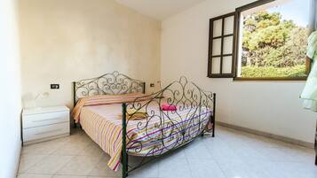 A single bed with a metal frame, a bedside table, and a window with a view of trees.