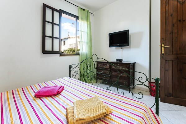 Une chambre à coucher avec un lit, une télévision, une fenêtre avec des rideaux, une porte en bois et une commode.