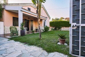 Une maison avec un patio en pierre, un petit jardin et un portail blanc.