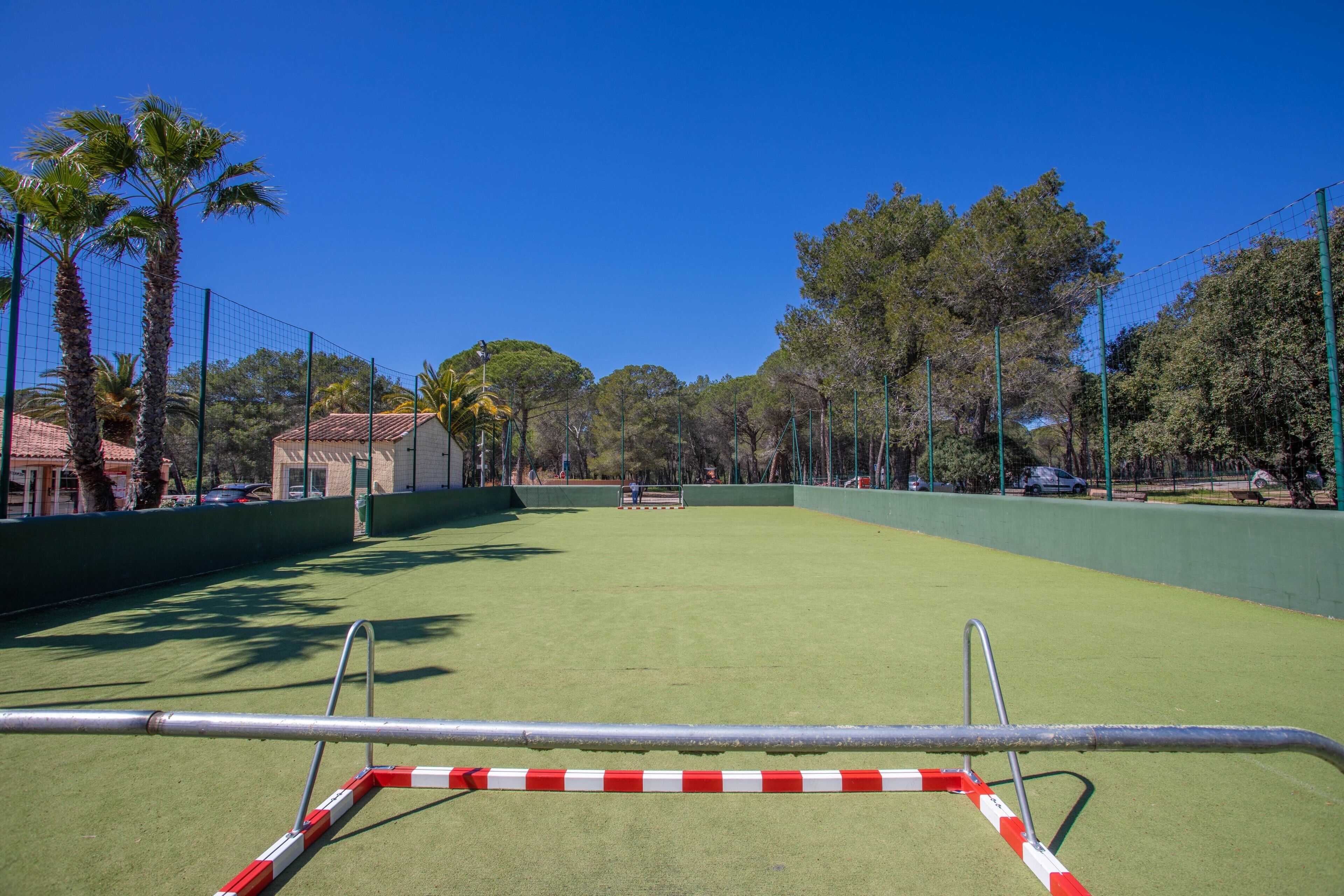 An outdoor tennis court with a net, surrounded by trees and a fence.