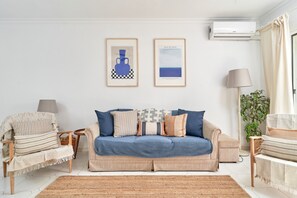 A living room with a sofa, armchairs, a lamp, and two framed artworks on the wall.