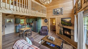 A spacious log cabin interior with a dining area, kitchen, living room, and a fireplace.