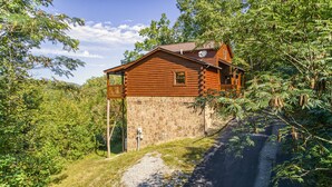 A log cabin with a stone foundation, a wooden deck, and a stone wall.