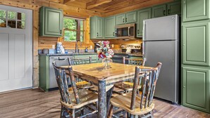 A rustic kitchen with wooden cabinets, a stainless steel refrigerator, and a wooden dining table with chairs.