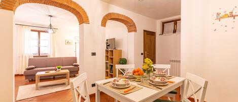 A dining area with a white table, green cushioned chairs, and a brick archway.