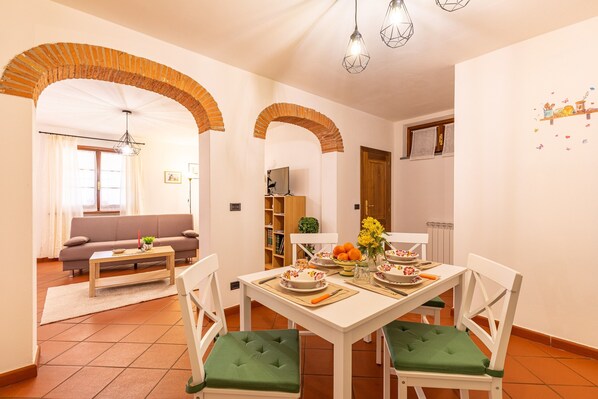 A dining area with a white table, green cushioned chairs, and a brick archway.