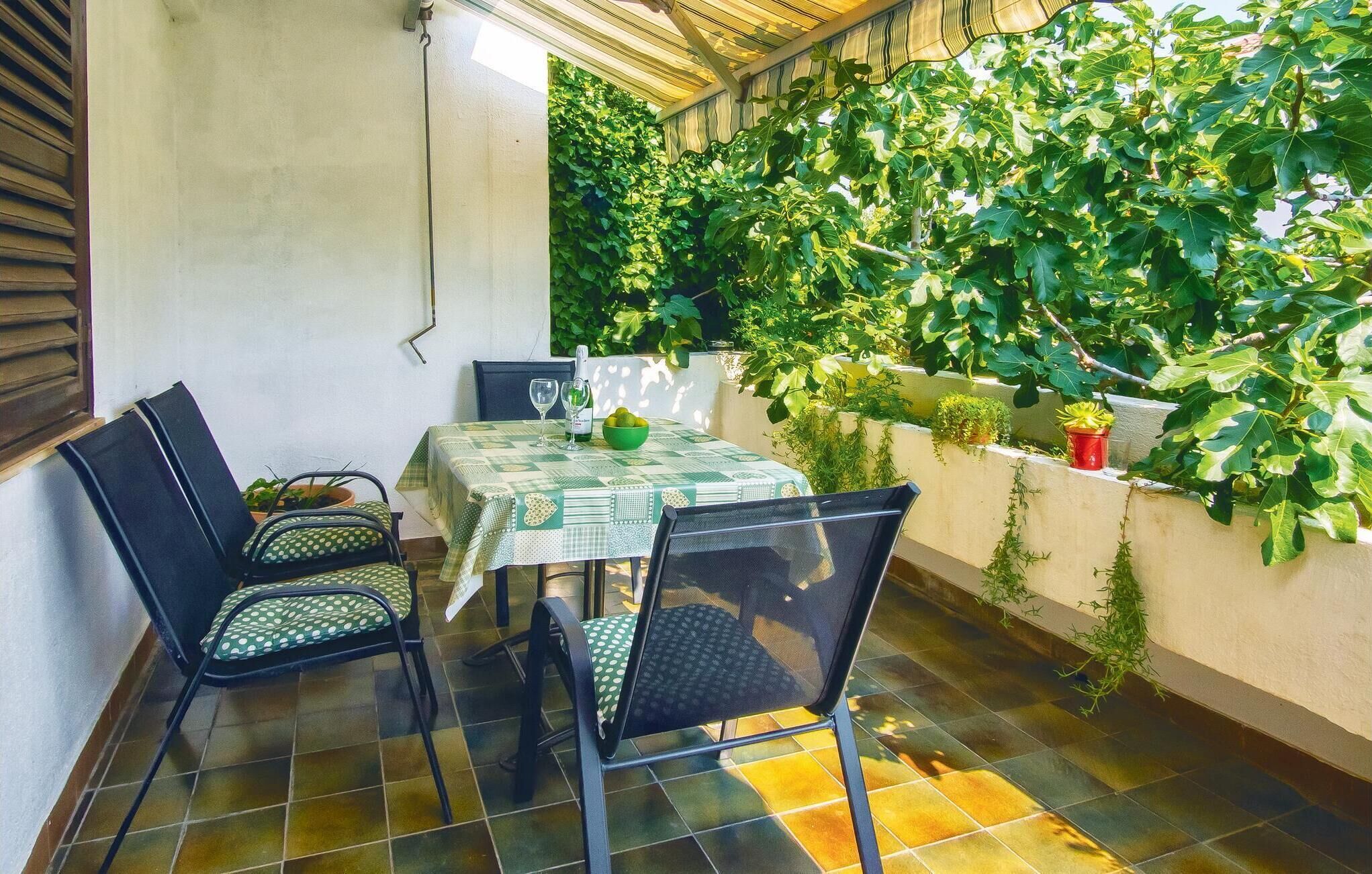 A patio with a table set for two, chairs, and a wall of greenery.