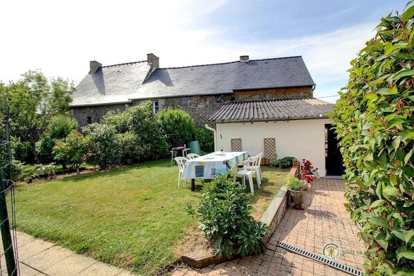 A stone house with a tiled roof, a small garden with a table and chairs, and a brick pathway. - La Chambre - Calorguen (CALORGUEN)