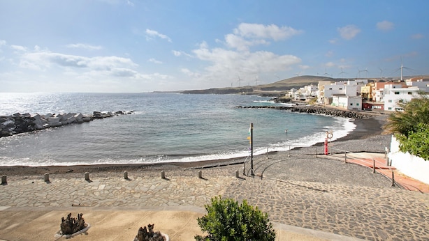 A coastal view with a stone-paved promenade, a beach, and buildings with wind turbines in the background. - Vacation Apartment 'Eras Views' with Sea View and Wi-Fi (Las eras)