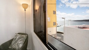 A room with a window, a chair, a lamp, and a view of a building and water. - Vacation Apartment 'Eras Views' with Sea View and Wi-Fi (Las eras)