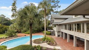 A pool surrounded by lush greenery and a covered patio area. - Monthly Stays Available! Pool/WalkToBeach/1MileToSaltyDog/LagoonSetting/Relaxing (Hilton Head Island)