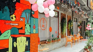 A colorful mural on a building, outdoor seating with orange chairs, and hanging decorations. - enjoy youth hotel (Wuhan)