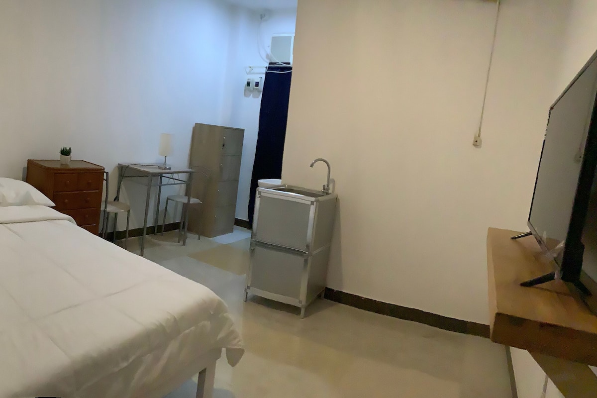 A hotel room with a bed, a desk, a small cabinet, and a television.