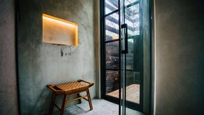 Habitación de esquina con pared de concreto, un taburete de madera, una puerta de vidrio que da al exterior y un aplique de pared.