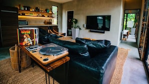 Una sala moderna con un sofá de cuero negro, una mesa de centro de madera y un reproductor de discos de vinilo. Hay un televisor montado en la pared y una estantería con diversos objetos.