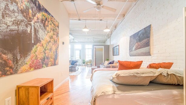 Een hotelkamer met een groot bed, een houten bankje, een schilderij en uitzicht op de stad.