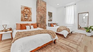 A modern bedroom with two beds, a brick accent wall, and a large mirror. - Two Level Apt: Dtwn Buffalo (Buffalo)