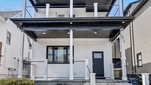 A two-story residential building with a covered front porch, a black door, and a visible staircase leading to the upper level. - Two Level Apt: Dtwn Buffalo (Buffalo)