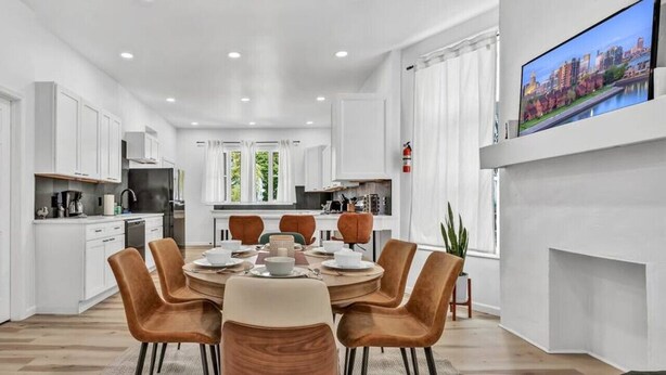 A modern kitchen with white cabinets, a dining area with a round table and chairs, and a TV mounted on the wall. - Two Level Apt: Dtwn Buffalo (Buffalo)