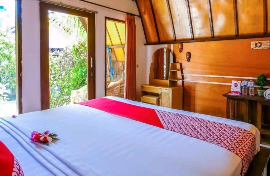 A hotel room with a bed, a wooden headboard, a desk with a chair, and a window with a view of greenery.