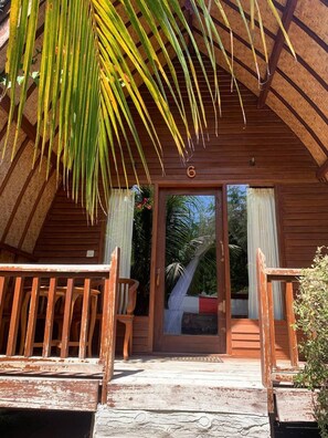 A wooden cabin with a thatched roof, a wooden porch with benches, and a door marked with the number 6. - Nelly Homestay (Gili Air)