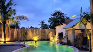Una piscina con cerramiento de madera y palmeras al fondo.
