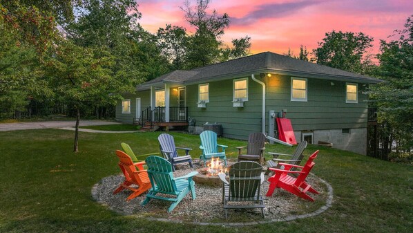 Uma casa com lareira e cadeiras Adirondack coloridas no quintal.