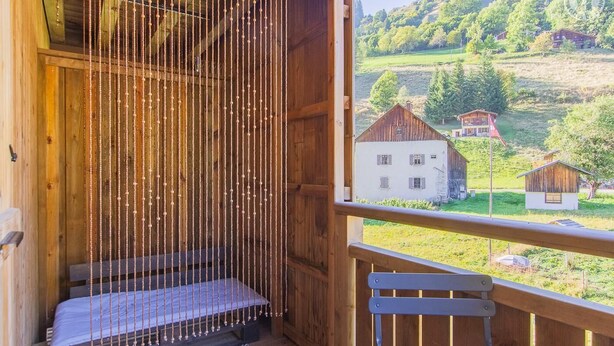 Un balcón de madera con un banco y vistas a un paisaje rural que incluye casas y follaje.