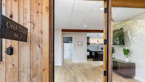 A wooden door with a sign reading "Creek Chalet no. 3" leading into a modern interior with a kitchen and dining area. - Creekside Getaway: On the Creek in Anchorage (Anchorage)