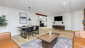 A modern living room with a dining area, a wooden coffee table, and a flat-screen TV mounted on the wall. - Creekside Getaway: On the Creek in Anchorage (Anchorage)