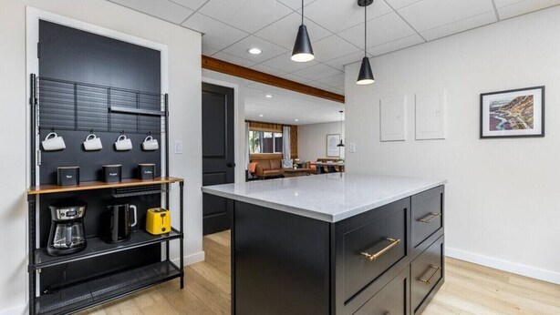A modern kitchen with a central island, black cabinetry, and a coffee station. - Creekside Getaway: On the Creek in Anchorage (Anchorage)