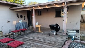 A backyard with a wooden deck, a barbecue grill, a small table, and a potted plant. - Comfortable for travelers tired of staying at hotels. (Kingman)